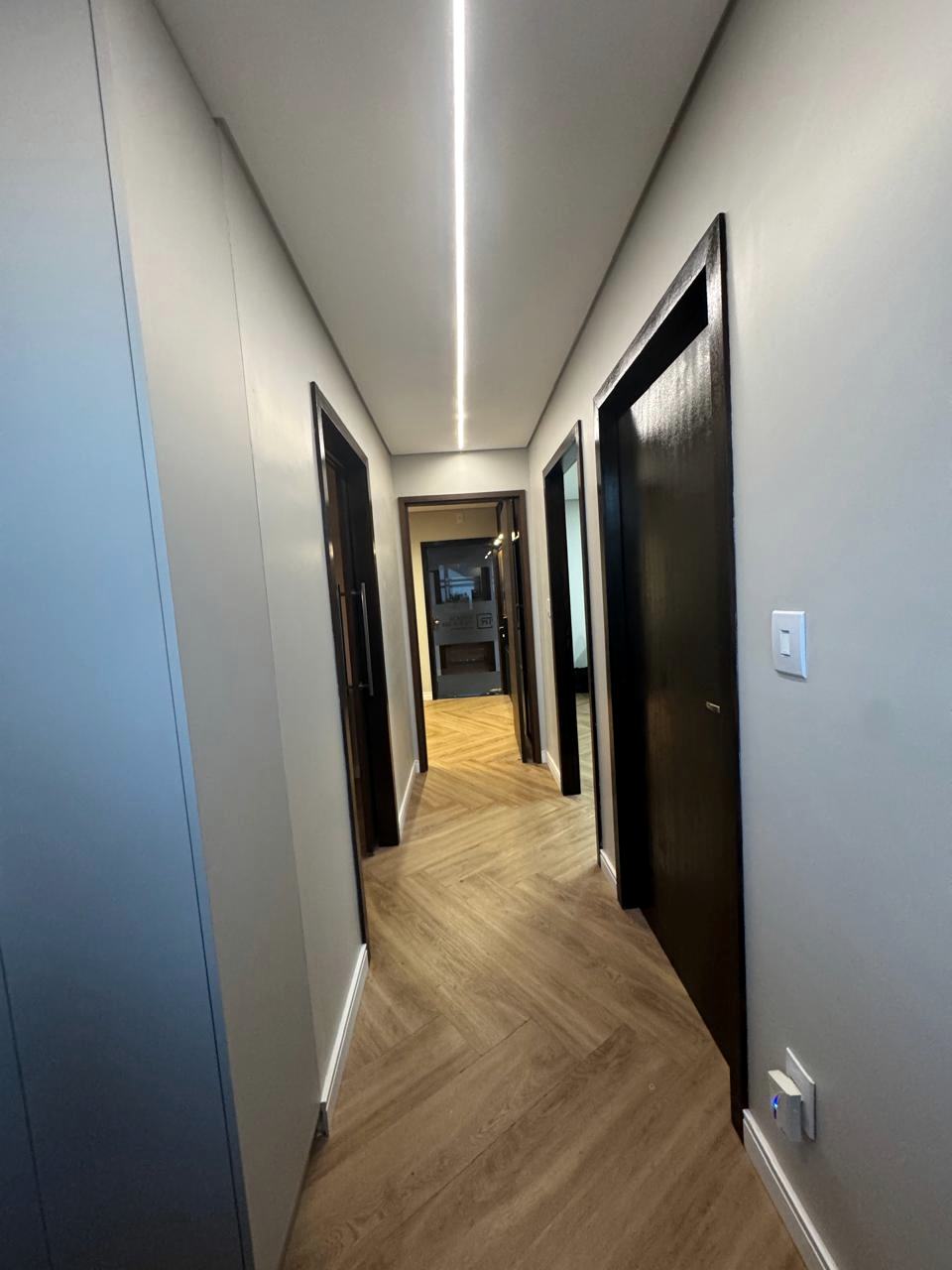 Corredor do escritório da Tatsch da Rocha Advogados, com piso de madeira e luz do teto