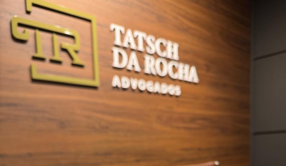 A logo da Tatsch da Rocha em latão sobre a parede de madeira do escritório